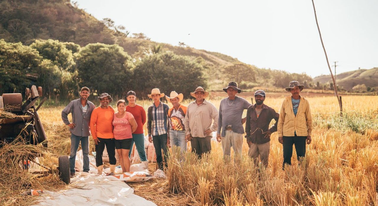 Grupo diverso de agricultores reunido em um campo ensolarado, representando o trabalho coletivo no meio rural.