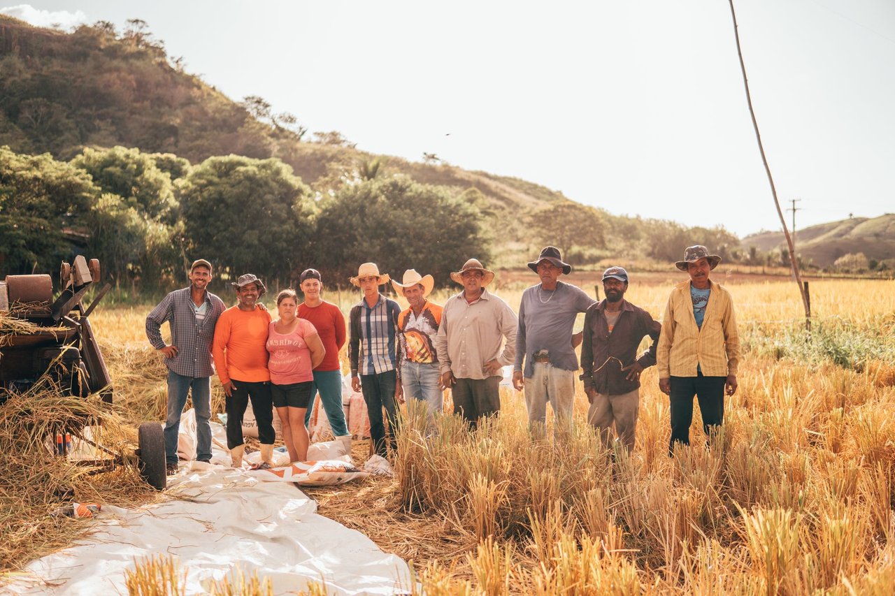 Grupo diverso de agricultores reunido em um campo ensolarado, representando o trabalho coletivo no meio rural.